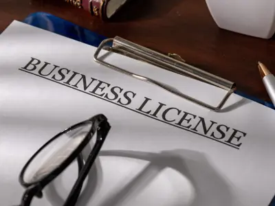 a clipboard with a piece of paper reading 'business license' and a pair of eyeglasses resting on top